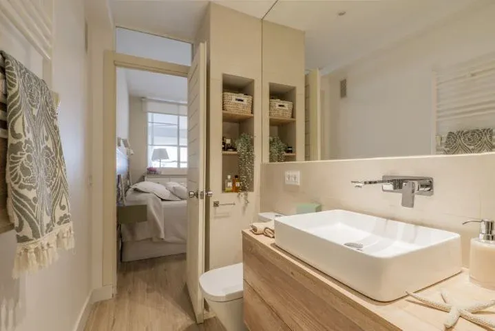 Salle de bain avec meuble-lavabo en bois, miroir sans cadre et alcôve avec étagères