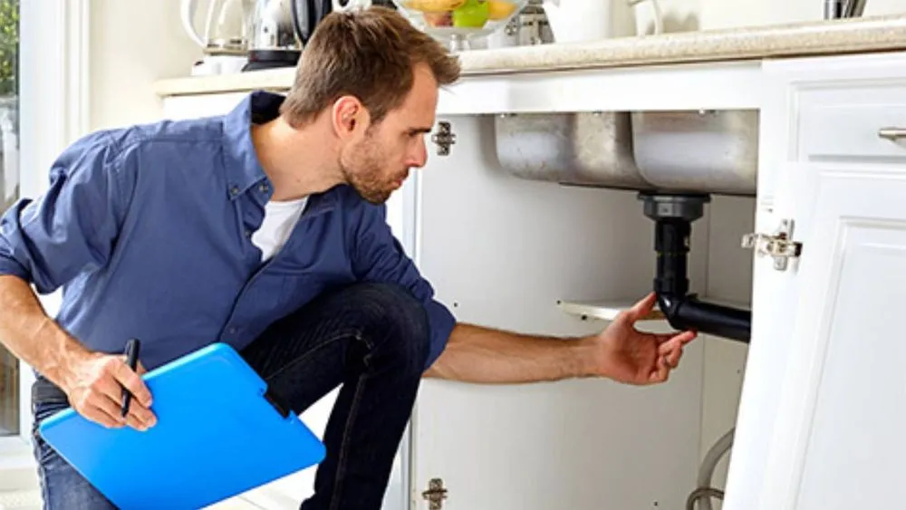 Un plombier expert inspectant des tuyauteries en cuivre avec une lampe torche, symbolisant le diagnostic plomberie pré-achat.